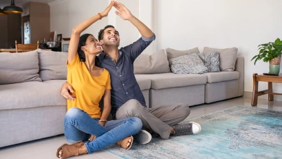 a couple sitting next to each other next to couch holding their hands together to make a house roof above them